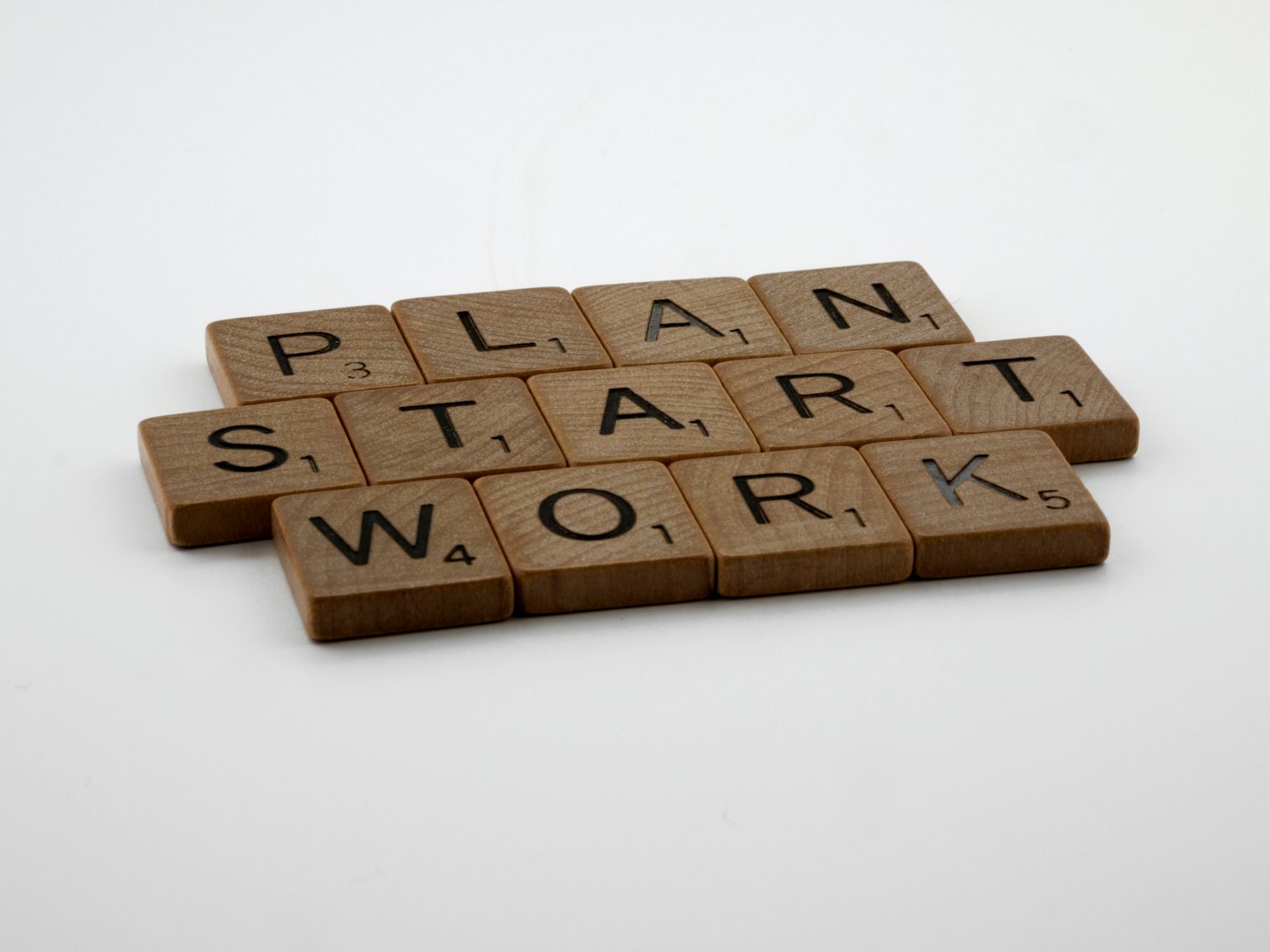 Drewniane klocki z literami układające napis 'PLAN START WORK' na białym tle.